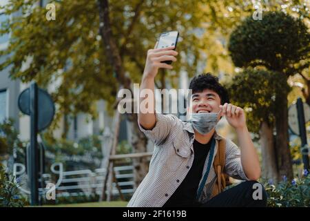 Homme asiatique portant un masque médical à l'aide d'une caméra de vidéoconférence avec smartphone et parlant avec ses amis ou sa famille pendant COVID-19. Social distenc Banque D'Images