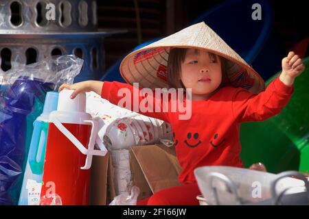 Jeune enfant vietnamien dans une cabine de marché portant des vêtements rouges et un chapeau conique de style vietnamien distinctif. Bac Ha, province Lao Cai, Vietnam Banque D'Images