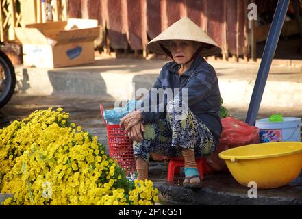 Femme vietnamienne en chapeau conique distinctif vendant des fleurs au marché de Hoi an, Vietnam Banque D'Images