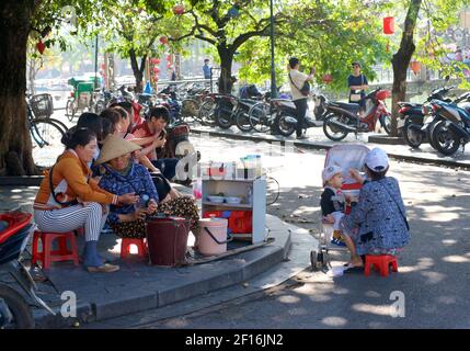 Vie de rue vietnamienne. Vendeurs vendant des collations sur le front de mer, Hoi an, Vietnam. Mère allaitant garçon en pram. Banque D'Images