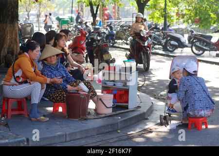 Vie de rue vietnamienne. Vendeurs vendant des collations sur le front de mer, Hoi an, Vietnam. Mère allaitant garçon en pram. Banque D'Images