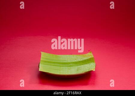 Feuille de banane, petit morceau de feuille de banane verte fraîche arrangé dans une assiette avec fond rouge texturé, isolé Banque D'Images