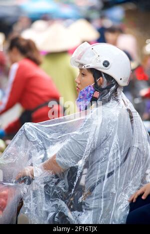 Femme en housse imperméable avec casque et masque sur moto. Hoi an, Vietnam Banque D'Images