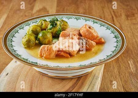 Saumon aux choux de Bruxelles, portion prête à l'emploi d'une recette étape par étape dans une assiette vintage sur fond de bois Banque D'Images