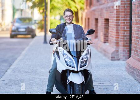 Heureux homme à bord d'un scooter dans la ville sur un jour ensoleillé Banque D'Images