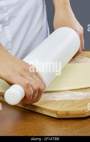 Étalez la main en gros plan de la pâte du boulanger du chef tablier bleu uniforme cuisez la pizza à la cuisine collection complète de recettes Banque D'Images