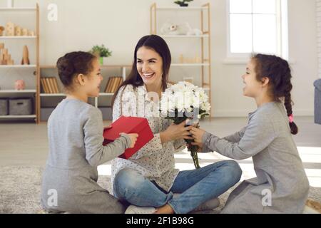 Heureuse femme souriante mère assise sur le sol entre ses filles et obtenir des fleurs et des cadeaux Banque D'Images