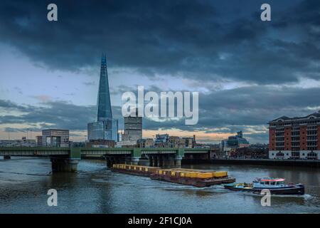 Une barge fluviale qui déplace des conteneurs contenant des déchets comme fret sur la voie navigable de la Tamise, le pont de Cannon Street, la ligne d'horizon du centre de Londres, au Royaume-Uni Banque D'Images