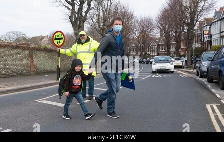 Brighton UK 8 mars 2021 - l'homme Lollipop Simon Moss accueille les enfants de retour à l'école primaire St Luke à Brighton ce matin, car les restrictions de verrouillage du gouvernement en Angleterre commencent à être assouplies . Les écoles et les collèges sont rouverts à tous les étudiants aujourd'hui dans toute l'Angleterre : crédit Simon Dack / Alamy Live News Banque D'Images