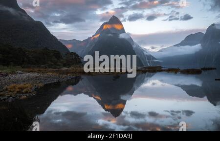 Les premiers rayons solaires éclairant le sommet de la montagne avec une belle réflexion dans la surface de l'eau en face de lui. Photo de Miter Peak au lever du soleil dans Milford Sound Banque D'Images