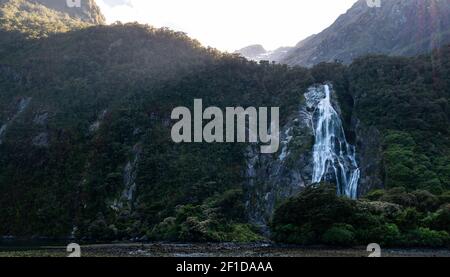 Photo rétro-éclairée de la cascade entourée de falaises vertes. L'emplacement est Lady Bowen Falls situé dans Milford Sound, Fiordland National Park, Nouvelle-Zélande Banque D'Images