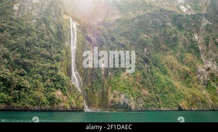 Immense cascade tombant de falaises vertes avec deux petits canoës au fond pour l'échelle. Il est situé à Stirling Falls, dans le Milford Sound, dans le parc national Fiordland Banque D'Images