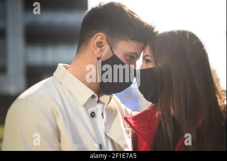 Romantique heureux jeune couple debout dans un regard étreinte dans les yeux des autres avec leurs avant-têtes se touchant et portant masques contre le coronavi Banque D'Images