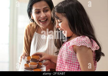 UNE FILLE HEUREUSE PRENANT DES PETITS GÂTEAUX DU PLATEAU CUIT PAR LA MÈRE Banque D'Images