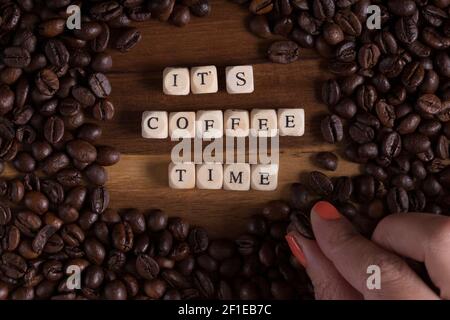 c'est l'heure du café avec un cube en bois lettres et et une main de femme avec un grain de café et du café tout autour sur une table en bois. bonjour. Banque D'Images