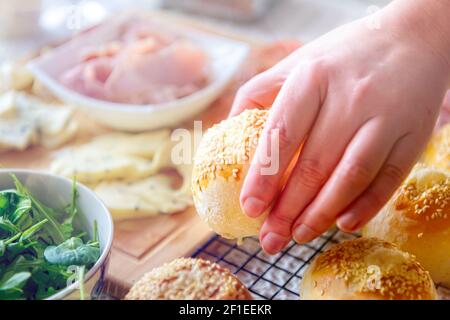 Petits pains faits maison aux graines de sésame. Une main de femme atteint pour un rouleau, une table avec le petit déjeuner Banque D'Images