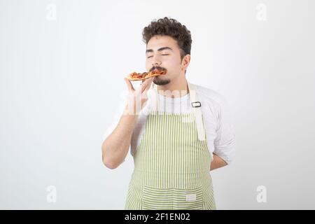 Image d'un homme cuisinier mangeant une tranche de pizza sur blanc arrière-plan Banque D'Images