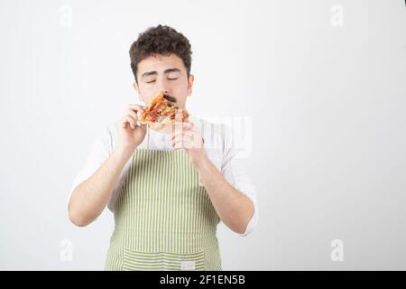 Image d'un homme cuisinier mangeant une tranche de pizza sur blanc arrière-plan Banque D'Images