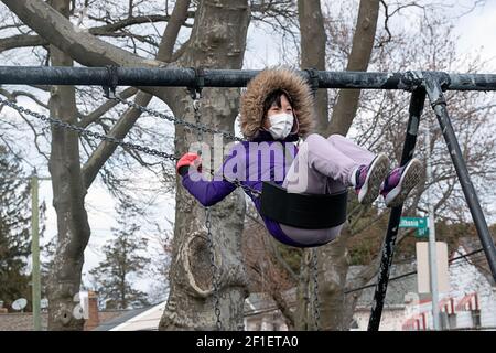 Un adolescent américain asiatique heureux masqué flis haut sur une balançoire à Kissena Park, Flushing, New York Banque D'Images