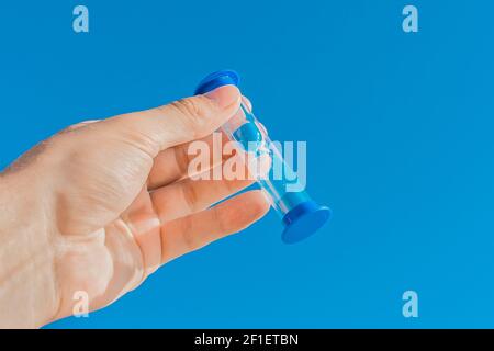 La main d'un homme tient un sablier sur un fond bleu ciel. Banque D'Images