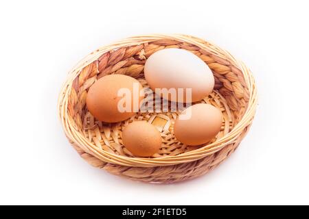 oeufs - quatre oeufs de poulet de différentes tailles dans un petit panier en osier, isolés sur fond blanc Banque D'Images