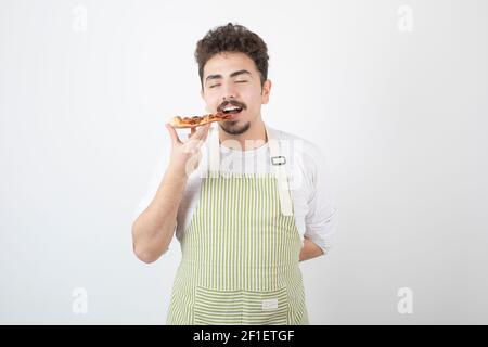 Image d'un homme cuisinier mangeant une tranche de pizza sur blanc arrière-plan Banque D'Images