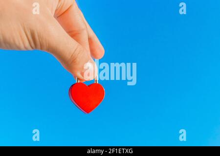 La main d'un homme tient un petit coeur rouge sous la forme d'un château de près contre le ciel bleu. Symbole et signe de l'amour. Banque D'Images