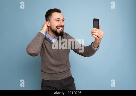 Photo d'un jeune brunette positif, jeune, non rasé, avec barbe porter un chandail gris décontracté et une chemise bleue isolée sur le rose maintien du mur d'arrière-plan Banque D'Images