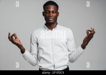 Jeune homme d'affaires méditant, yeux fermés, isolé sur fond de mur gris. Concept des techniques de soulagement de stress au travail Banque D'Images