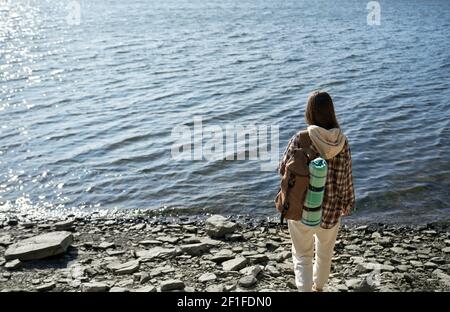 Jeune femme avec des cheveux bruns randonnée avec sac à dos au canyon de Dniester. Joyeux touriste dans une tenue décontractée debout près de l'eau et de prendre la pause. Banque D'Images