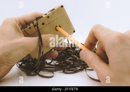 Les mains de l'homme rembobinent manuellement le film audio magnétique dans la cassette dorée avec un crayon . Style de couleur vintage Banque D'Images