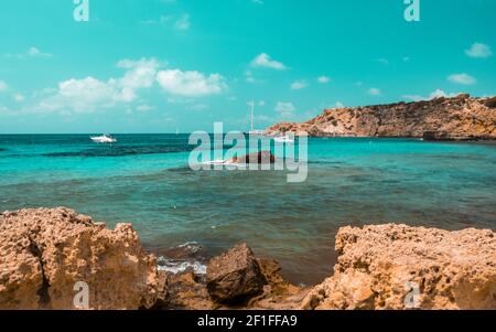 Ambiance sarcelle et orange de la plage de Cala Tarida avec pierres, île d'Ibiza. Espagne Banque D'Images