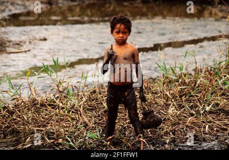 Un jeune garçon dans la boue profonde de la chasse au ricow de sa famille pour les crabes, dans le sud rural du Vietnam, juin 1980 Banque D'Images