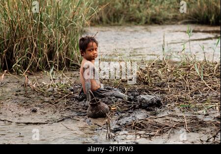 Un jeune garçon dans la boue profonde de la chasse au ricow de sa famille pour les crabes, dans le sud rural du Vietnam, juin 1980 Banque D'Images