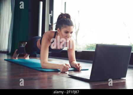 Jeune entraîneur personnel instructeur de fitness faisant cours en ligne par ordinateur portable montrant l'exercice de planche pendant les pandémies Banque D'Images