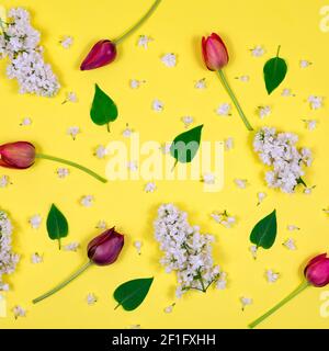 Tulipes rouges, lilas blanc et feuilles vertes sur fond jaune. Vue de dessus. Vide pour une carte postale. Fête des mères, Saint-Valentin, anniversaire Banque D'Images