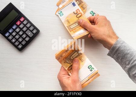 Homme remet en main le comptage des billets de banque en euros et la calculatrice table blanche Banque D'Images