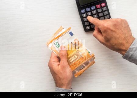 Homme remet en main le comptage des billets de banque en euros et la calculatrice table blanche Banque D'Images