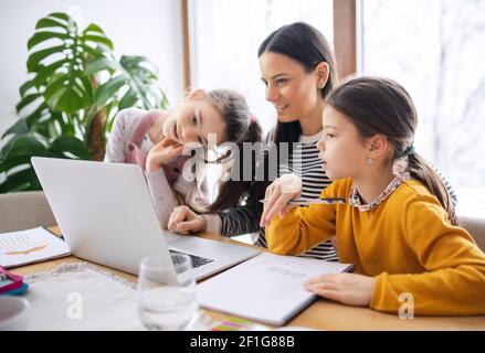 Mère avec des filles d'école à l'intérieur à la maison, l'apprentissage à distance et le bureau à domicile. Banque D'Images