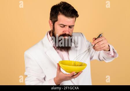 Homme barbu préparant des œufs pour le petit déjeuner. Fouettez l'œuf dans un bol pour faire cuire l'omelette ou la pâte. Outil de cuisine, cuisine et concept de cuisine. Banque D'Images