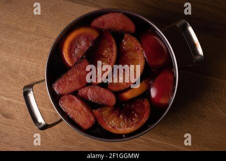 Vin rouge vin chaud avec pommes et oranges dans le processus de fabrication à la maison dans une casserole en acier inoxydable. Banque D'Images