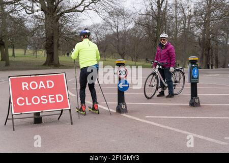 Une femme cycliste regarde un homme skieur à roulettes à travers dedans Entre les bornes du London Greenwich Park Banque D'Images