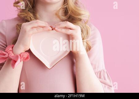 Gros plan sur une fille avec une soucoupe en forme de coeur sur fond rose. Banque D'Images