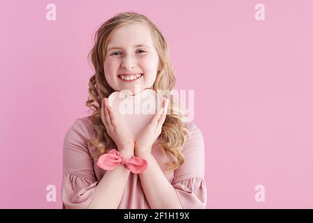 Portrait d'un enfant moderne heureux en robe rose avec soucoupe en forme de coeur isolée sur fond rose. Banque D'Images