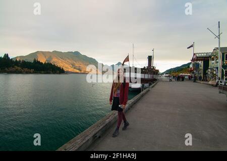 Voyagez avec une femme touristique au coucher du soleil à Queenstown quai avec bateau à vapeur sur le lac Wakatipu en arrière-plan, Nouvelle-Zélande, Île du Sud Banque D'Images