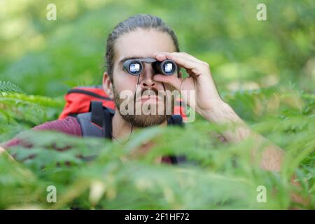 randonneur mâle regardant à travers des jumelles dans la forêt Banque D'Images