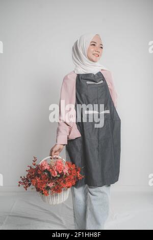 modèle portant le hijab tenant une fleur sur fond beige. Femelle musulmane tenant un seau de fleur Banque D'Images