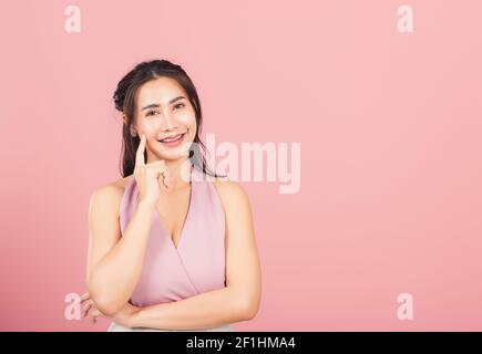 Portrait asiatique belle jeune femme souriante debout menton poignée détendue en pensant à la question sur laquelle le studio a tourné isolé bac rose Banque D'Images