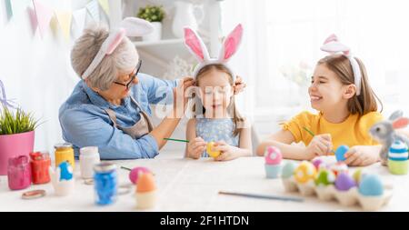 Une grand-mère et ses petites-filles peignant des œufs. Bonne famille se préparant pour Pâques. Les petites filles adorables portent des oreilles de lapin. Banque D'Images