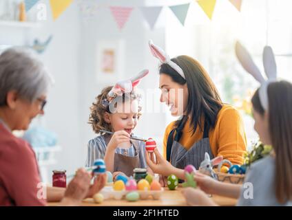 La mère, le grand-mère et les enfants peignent des œufs. Une famille heureuse se prépare pour Pâques. Petites filles mignonnes portant des oreilles de lapin. Banque D'Images